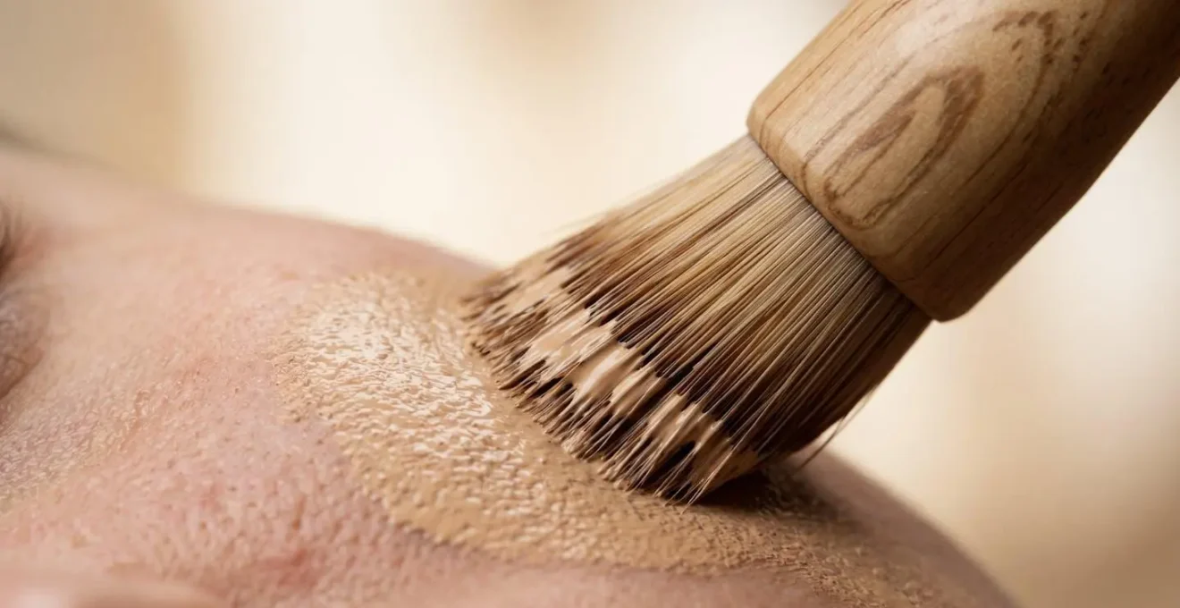 Dettaglio macro di pennello da trucco che applica fondotinta su pelle naturale con texture realistica e luce morbida