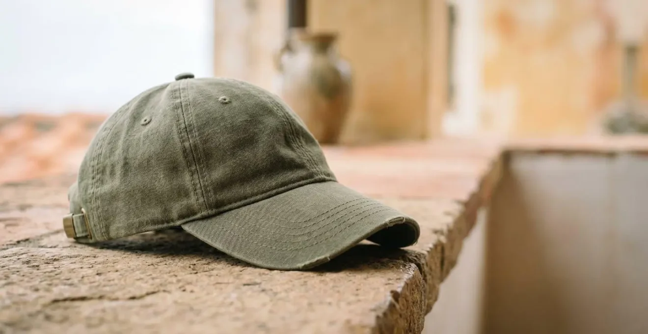 Cappellino con visiera curva su superficie naturale che richiama l'eleganza informale italiana