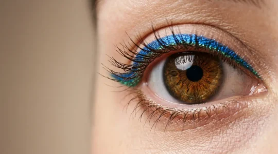 Dettaglio ravvicinato di occhi castani con eyeliner blu elettrico e verde smeraldo che esaltano l'iride