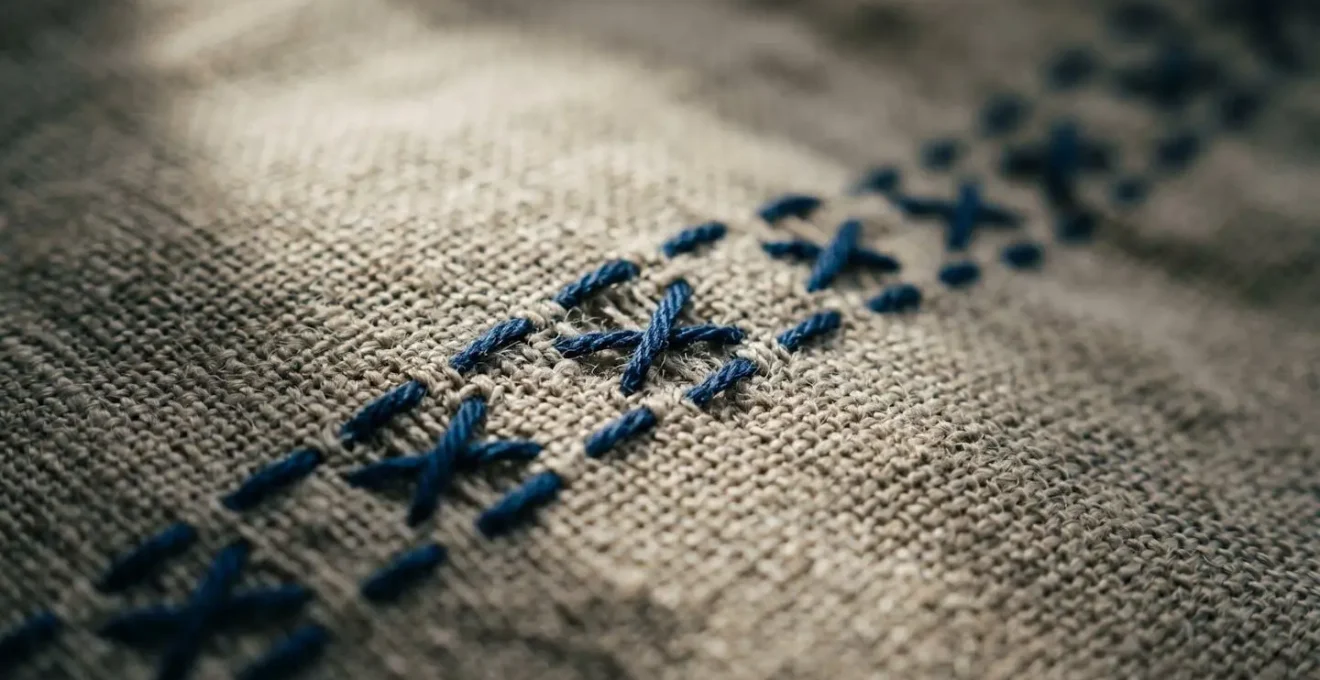 Dettaglio macro di un rammendo artigianale su tessuto naturale con punto visible mending in filo contrastante