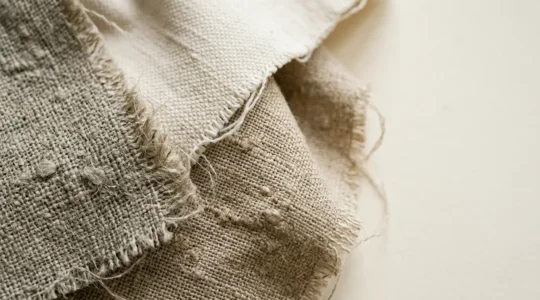 Primo piano di tessuti naturali con texture visibili e dettagli artigianali su sfondo minimalista